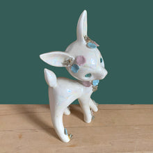 Load image into Gallery viewer, Adorable vintage mid-century era anthropomorphic deer ceramic figurine, glazed in iridescent white with blue rhinestone eyes, pink and blue flowers and gold gilt spaghetti details. Crafted by Lefton, Japan, circa 1950s. This sweet-faced deer is sure to delight everyone and it will make a wonderful addition to your Christmas holiday decor!
In good vintage condition. There is a chip to one blue flower, but otherwise excellent. Marked Japan and number 5845.
Measures 3 1/2 x 2 1/2 x 7 inches