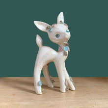 Load image into Gallery viewer, Adorable vintage mid-century era anthropomorphic deer ceramic figurine, glazed in iridescent white with blue rhinestone eyes, pink and blue flowers and gold gilt spaghetti details. Crafted by Lefton, Japan, circa 1950s. This sweet-faced deer is sure to delight everyone and it will make a wonderful addition to your Christmas holiday decor!
In good vintage condition. There is a chip to one blue flower, but otherwise excellent. Marked Japan and number 5845.
Measures 3 1/2 x 2 1/2 x 7 inches