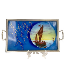 Load image into Gallery viewer, Stunning art deco reverse painted tray with metal frame and handles. Depicts sailboats on the water within a circle on a royal blue background with gold trailing leaves lending itself nicely to a Hollywood Regency or Chinoiserie decor. Germany, 1920s. Perfect as a vanity tray, service barware or even wall art.
The painting is in excellent condition with age-related wear to the frame.
Measures 14 1/8 x 8 3/4 (not incl. handles)