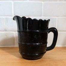 Load image into Gallery viewer, RARE! Gothic Victorian black pressed glass creamer jug. The lower 2/3 are stippled between smooth bands, while the top 1/3 is smooth. Produced by Davidson's, England, c1890 - 1910. A great piece to start a collection! In excellent vintage condition, free from chips/cracks/repairs. There is a manufacturer's defect on the underside of the foot near the mold line. Measures 2 3/4 x 3 1/2 inches (not including handle)