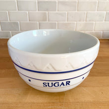 Load image into Gallery viewer, Angled overhead view of vintage-style blue and white ceramic mixing bowl showing the smooth white interior, rolled rim with blue decorative band, and embossed exterior detail