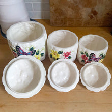Load image into Gallery viewer, Rare set of three vintage mid-century white figural pumpkin squash ceramic canisters. These three dimensional beauties are hand painted with colourful butterflies and flowers. Each lid is topped with a floral finial. Enterprise Sales & Distributors import, Japan, 1960s. Perfect for the kitchen kitsch collectible enthusiast!