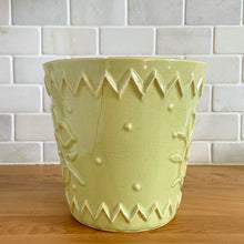 Load image into Gallery viewer, Rare vintage chartreuse green planter pot with embossed flower motif and zig zag borders. Crafted by McCoy Pottery, 1954. This rare planter is must for any McCoy art pottery collector. A wonderful piece to elevate your home and garden decor or to give as a gift!
In as found vintage condition, chip to the rim and crack, no repairs. Normal age-related crazing and manufacturer's glaze pops. Maker's mark on the bottom.
Measures 6 1/2 x 6 1/8 inches