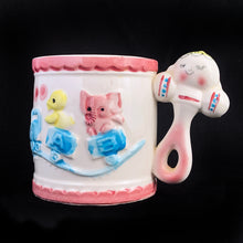 Load image into Gallery viewer, Kitschy cuteness abounds in this vintage mid-century ceramic child's mug featuring a figural baby faced rattle along with an embossed train on its track with a sweet yellow chick and pink elephant in alphabet cars, rimmed in pink scalloped borders at the top and bottom. Crafted by Rubens, Japan, circa 1950s. Such a sweet piece for a nursery and would make a lovely baby shower gift!