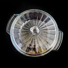 Load image into Gallery viewer, This large vintage clear glass lidded casserole dish has a distinctive scalloped design that makes cooking and serving effortless. It is oven, microwave, and dishwasher safe, making it easy to transport and reheat your favorite dishes with minimal mess. Crafted by Anchor Hocking, USA, circa 1950s, this dish is sure to bring style and convenience to your kitchen. In excellent condition, free from chips. Measures 9 inches / 23 cm Capacity 2 quarts/litres