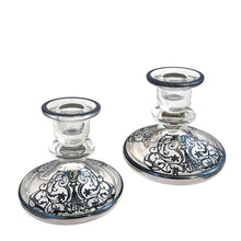 Load image into Gallery viewer, Stunning pair of vintage clear glass single lite candle holders featuring a silver overlay pattern with urn and floral scrolls. Silver City, 1950s. A romantic addition to your tablescape!
In vintage condition, the silver overlay is intact. There is a smooth chip to one piece, see photos.
Measures 4 1/4 x 4 1/4 x 3 3/4 inches
