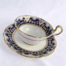 Load image into Gallery viewer, Antique bone china teacup and saucer is absolutely stunning! Both have a subtle scalloped shape. The white cup is decorated in a design of pale blue floral bouquets and bows on a cobalt blue band with gold gilt details. Produced by Aynsley, England. Excellent condition, free from chips, cracks and repairs. The pattern number 3410 is painted on the saucer. The stamped maker's mark indicates production between 1905 - 1925. Teacup measures 3 1/2 x 2 1/4 inches | Saucer measures 5 5/8 inches