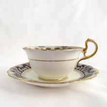 Load image into Gallery viewer, Antique bone china teacup and saucer is absolutely stunning! Both have a subtle scalloped shape. The white cup is decorated in a design of pale blue floral bouquets and bows on a cobalt blue band with gold gilt details. Produced by Aynsley, England. Excellent condition, free from chips, cracks and repairs. The pattern number 3410 is painted on the saucer. The stamped maker's mark indicates production between 1905 - 1925. Teacup measures 3 1/2 x 2 1/4 inches | Saucer measures 5 5/8 inches
