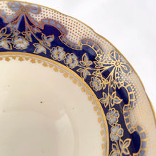 Load image into Gallery viewer, Antique bone china teacup and saucer is absolutely stunning! Both have a subtle scalloped shape. The white cup is decorated in a design of pale blue floral bouquets and bows on a cobalt blue band with gold gilt details. Produced by Aynsley, England. Excellent condition, free from chips, cracks and repairs. The pattern number 3410 is painted on the saucer. The stamped maker's mark indicates production between 1905 - 1925. Teacup measures 3 1/2 x 2 1/4 inches | Saucer measures 5 5/8 inches