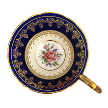 Load image into Gallery viewer, Vintage Bone China teacup and saucer with scalloped edge features a hand painted cobalt blue and pale yellow banded interior on a white ground, lavishly decorated with gold gilt filigree, complemented by pink cabbage roses at the bottom of the cup and centre of the saucer. Aynsley, England. 1930s. In excellent condition. Maker's mark with decorator's hand painted C553 Teacup measures 4 x 2 1/4 inches Saucer measures 5 5/8 inches