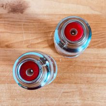 Load image into Gallery viewer, These shakers give off all the vintage vibes! Pressed clear glass of concentric circles or stacked rings on a round foot with silver-toned metal lids plus interior red disc. Part of Line #3530, produced by Hazel-Atlas Glass, USA, circa 1930s. In excellent condition, free from chips/cracks. Normal age-related wear. Marked "Anko" on the bottom Measures 3 1/2 inches tall