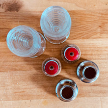 Load image into Gallery viewer, These shakers give off all the vintage vibes! Pressed clear glass of concentric circles or stacked rings on a round foot with silver-toned metal lids plus interior red disc. Part of Line #3530, produced by Hazel-Atlas Glass, USA, circa 1930s. In excellent condition, free from chips/cracks. Normal age-related wear. Marked "Anko" on the bottom Measures 3 1/2 inches tall