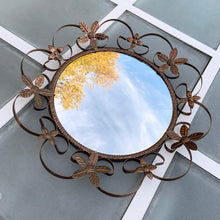 Load image into Gallery viewer, Bring on the mid-century vintage vibes with this round convex mirror encased in copper toned metal featuring a pierced metal band, surrounded with scrolled metal sections and impressed metal flowers. The mirror has a wood backing and a built in wall hanger. Circa 1950s. This beauty is ready to hang and is sure to add a special touch of glam to your bath, bedroom or entranceway! In excellent condition. Measures 17 1/2 inches in diameter