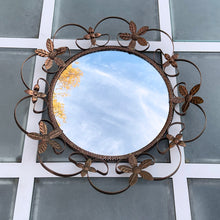 Load image into Gallery viewer, Bring on the mid-century vintage vibes with this round convex mirror encased in copper toned metal featuring a pierced metal band, surrounded with scrolled metal sections and impressed metal flowers. The mirror has a wood backing and a built in wall hanger. Circa 1950s. This beauty is ready to hang and is sure to add a special touch of glam to your bath, bedroom or entranceway! In excellent condition. Measures 17 1/2 inches in diameter