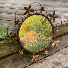 Load image into Gallery viewer, Bring on the mid-century vintage vibes with this round convex mirror encased in copper toned metal featuring a pierced metal band, surrounded with scrolled metal sections and impressed metal flowers. The mirror has a wood backing and a built in wall hanger. Circa 1950s. This beauty is ready to hang and is sure to add a special touch of glam to your bath, bedroom or entranceway! In excellent condition. Measures 17 1/2 inches in diameter