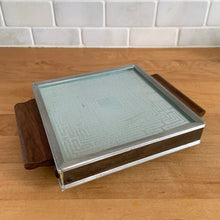 Load image into Gallery viewer, Vintage mid-century square Cosmopolitan Automatic Food Warmer with wood handles and a geometric surface. Salton, USA, 1960s. At any family dinner, my grandmother used her vintage Salton tray to keep all her yummy dishes hot. This one is perfectly sized for a coffee or tea pot and is small enough to be used on a desk or side table to keep your hot beverage warm.
In overall excellent vintage condition, no chips or cracks in the glass top. Good working order with cord.
Measures 8 1/4 x 6 1/4 inches