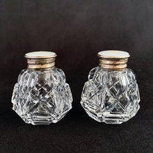 Load image into Gallery viewer, A pair of traditional vintage round paneled shaped cut crystal salt and pepper shakers in the art deco style featuring an "X" and diamond pattern with sterling silver mother-of-pearl lids.   In excellent condition, no chips or cracks. Marked 925 Sterling.  Measures 1 1/2 x 1 3/4 inches