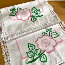 Load image into Gallery viewer, A lovely vintage white cotton dresser scarf or table runner, featuring a sweet hand embroidered pink flowers and green leaves with a pink inner border and beautifully crocheted edge. A gorgeous addition to your linen collection! In good used vintage condition, free from tears, minor stain. Measures 34 1/2 x 15 inches