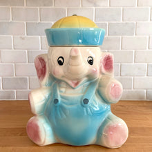 Load image into Gallery viewer, Vintage mid-century hand painted figural white elephant ceramic cookie jar with blue and yellow sailor hat and overalls and pink details. Crafted by American Bisque, USA, circa 1950s. Add some kitsch to your kitchen decor with this adorable collectible!
In excellent condition, no chips or cracks, age-related crazing. Marked USA on the back of the jar.
Measures 8 1/2 x 6 x 10 1/2 inches