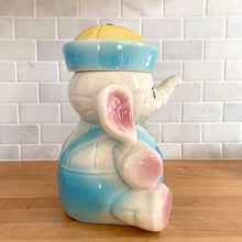 Load image into Gallery viewer, Vintage mid-century hand painted figural white elephant ceramic cookie jar with blue and yellow sailor hat and overalls and pink details. Crafted by American Bisque, USA, circa 1950s. Add some kitsch to your kitchen decor with this adorable collectible!
In excellent condition, no chips or cracks, age-related crazing. Marked USA on the back of the jar.
Measures 8 1/2 x 6 x 10 1/2 inches