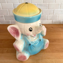 Load image into Gallery viewer, Vintage mid-century hand painted figural white elephant ceramic cookie jar with blue and yellow sailor hat and overalls and pink details. Crafted by American Bisque, USA, circa 1950s. Add some kitsch to your kitchen decor with this adorable collectible!
In excellent condition, no chips or cracks, age-related crazing. Marked USA on the back of the jar.
Measures 8 1/2 x 6 x 10 1/2 inches