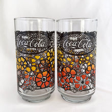 Load image into Gallery viewer, Vintage retro Coca-Cola promotional glass featuring a colourful flower power graphic illustration in an ombre of red, orange and yellow outlined in black. The word "Enjoy" sits above the distinctive Coke logo in a oval medallion reminiscent of a stained glass window. Makers mark is impressed on the bottom, however, we're unable to assign it to a specific maker. In excellent, like new condition, free from chips.
