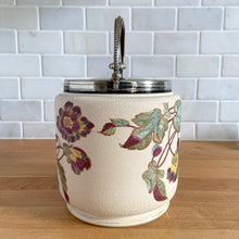 Load image into Gallery viewer, Antique porcelain biscuit jar featuring whimsical florals on a cream ground with silver plated collar, handle and lid. Crafted by Taylor Tunnicliffe, England, 1875 - 1898. Absolutely stunning example of decorative and functional artistry from the Aesthetic Movement era! In overall excellent condition for a piece of its age with wear to the silver plate on the lid and minor discolouration on the porcelain. Measures 5 x 6 5/8 inches (8 1/4 with handle raised)