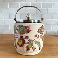 Load image into Gallery viewer, Antique porcelain biscuit jar featuring whimsical florals on a cream ground with silver plated collar, handle and lid. Crafted by Taylor Tunnicliffe, England, 1875 - 1898. Absolutely stunning example of decorative and functional artistry from the Aesthetic Movement era! In overall excellent condition for a piece of its age with wear to the silver plate on the lid and minor discolouration on the porcelain. Measures 5 x 6 5/8 inches (8 1/4 with handle raised)