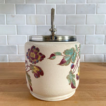 Load image into Gallery viewer, Antique porcelain biscuit jar featuring whimsical florals on a cream ground with silver plated collar, handle and lid. Crafted by Taylor Tunnicliffe, England, 1875 - 1898. Absolutely stunning example of decorative and functional artistry from the Aesthetic Movement era! In overall excellent condition for a piece of its age with wear to the silver plate on the lid and minor discolouration on the porcelain. Measures 5 x 6 5/8 inches (8 1/4 with handle raised)