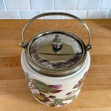 Load image into Gallery viewer, Antique porcelain biscuit jar featuring whimsical florals on a cream ground with silver plated collar, handle and lid. Crafted by Taylor Tunnicliffe, England, 1875 - 1898. Absolutely stunning example of decorative and functional artistry from the Aesthetic Movement era! In overall excellent condition for a piece of its age with wear to the silver plate on the lid and minor discolouration on the porcelain. Measures 5 x 6 5/8 inches (8 1/4 with handle raised)