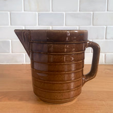 Load image into Gallery viewer, Vintage glossy caramel brown stoneware pitcher with horizontal ribbed detail. Crafted by Monmouth Western Stoneware, USA, 1920s. Add this utilitarian piece to your farmhouse decor or art pottery collection!
In excellent condition, no chips/cracks/repairs, age-related crazing. Unmarked.
Measures 4 1/2 x 5 inches