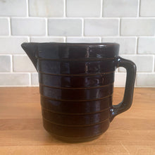 Load image into Gallery viewer, Vintage glossy deep brown stoneware pitcher with horizontal ribbed detail. Crafted by Monmouth Western Stoneware, USA, 1920s. Add this utilitarian piece to your farmhouse decor or art pottery collection!
In excellent condition, no chips/cracks/repairs, age-related crazing. Unmarked.
Measures 4 1/2 x 5 inches