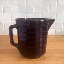 Load image into Gallery viewer, Vintage glossy deep brown stoneware pitcher with horizontal ribbed detail. Crafted by Monmouth Western Stoneware, USA, 1920s. Add this utilitarian piece to your farmhouse decor or art pottery collection!
In excellent condition, no chips/cracks/repairs, age-related crazing. Unmarked.
Measures 4 1/2 x 5 inches
