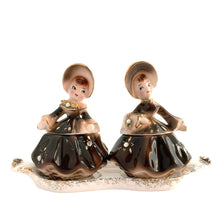 Load image into Gallery viewer, Vintage hand painted Golden Girl ceramic condiment set with tray. Enesco, Japan, 1960s. Add this pretty set to your collection!
In excellent condition, no chips/cracks/repairs.
Each girl measures 2 1/2 x 1 7/8 x 3 1/2 inches
Tray measures 6 1/4 x 2 1/8 inches