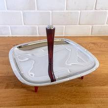 Load image into Gallery viewer, Straight out of the atomic age, this "Gourmates" chrome single tier serving tidbit tray with amber Bakelite legs and handle delivers loads of mid-century modern vibe to entertaining. This piece appears to be new old stock and is super shiny. Produced by Glo-Hill in Canada, circa 1960s. A stylish way to serve anything from appetizers to chocolates! In excellent condition and looks brand spanking new! Measures 7 1/8 x 7 1/8 x 4 3/4 inches