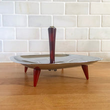 Load image into Gallery viewer, Straight out of the atomic age, this "Gourmates" chrome single tier serving tidbit tray with amber Bakelite legs and handle delivers loads of mid-century modern vibe to entertaining. This piece appears to be new old stock and is super shiny. Produced by Glo-Hill in Canada, circa 1960s. A stylish way to serve anything from appetizers to chocolates! In excellent condition and looks brand spanking new! Measures 7 1/8 x 7 1/8 x 4 3/4 inches