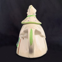 Load image into Gallery viewer, Vintage cream coloured figural "Granny Ann" ceramic teapot featuring a sweet granny holding a brown cane and dressed in a hat and garden frock in green and purple. Crafted by Shawnee Pottery, USA, circa 1940s. Even the spout is a figural basket! In excellent condition, free from chips/cracks/repairs. Marked on the bottom, "Patented Granny Ann U.S.A." Measures 8 x 5 5/8 x 8 1/2 inches