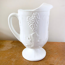 Load image into Gallery viewer, The words "stunning" and "elegant" embody this incredible milk glass pitcher in the "Harvest" pattern of grapes and vines. This is the largest version in this series holding 72oz. Made by Colony (Indiana) Glass Co. Circa 1966. This pitcher would look amazing on any tablescape or use it for a beautiful floral bouquet. In excellent condition, no chips or cracks. Measures 6 x 10 3/8 inches