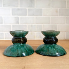 Load image into Gallery viewer, Front view of the pair side by side against white subway tile, showing the full hourglass profile: wide flared base, dark bulbous middle, and green drip glaze top cup