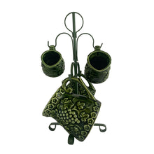 Load image into Gallery viewer, Vintage set of four dark green glazed ceramic measuring cups which hang on a green metal stand. Crafted by Noritake, Japan, 1960s. The cups feature an embossed grapevine pattern with flower borders. Each cup is marked, 1 cup, 1/2 cup, 1/4 cup and 1/8 cup. A sweet and practical piece of kitchen decor! Overall good vintage condition. The 1/2 cup has a glaze chip on the rim and the 1/4 cup measure has a tiny flea bite on the handle, see photos.