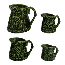 Load image into Gallery viewer, Vintage set of four dark green glazed ceramic measuring cups which hang on a green metal stand. Crafted by Noritake, Japan, 1960s. The cups feature an embossed grapevine pattern with flower borders. Each cup is marked, 1 cup, 1/2 cup, 1/4 cup and 1/8 cup. A sweet and practical piece of kitchen decor! Overall good vintage condition. The 1/2 cup has a glaze chip on the rim and the 1/4 cup measure has a tiny flea bite on the handle, see photos.
