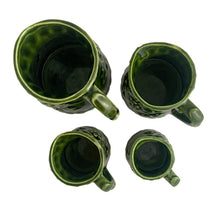 Load image into Gallery viewer, Vintage set of four dark green glazed ceramic measuring cups which hang on a green metal stand. Crafted by Noritake, Japan, 1960s. The cups feature an embossed grapevine pattern with flower borders. Each cup is marked, 1 cup, 1/2 cup, 1/4 cup and 1/8 cup. A sweet and practical piece of kitchen decor! Overall good vintage condition. The 1/2 cup has a glaze chip on the rim and the 1/4 cup measure has a tiny flea bite on the handle, see photos.