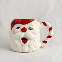 Load image into Gallery viewer, A hand painted vintage happy Santa Claus ceramic mug decorated in red, white, green and black plus a candy cane striped handle! Crafted in Taiwan, circa 1980s. Add charm to your Christmas decor by filling this adorable mug with candy canes! In excellent vintage condition, free from chips/cracks/repairs with one minor spot of glaze loss on the green holly leaf. Measures 3 1/2 x 3 1/4 inches