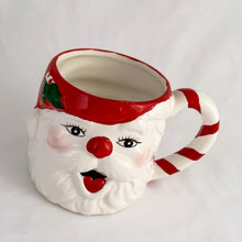 Load image into Gallery viewer, A hand painted vintage happy Santa Claus ceramic mug decorated in red, white, green and black plus a candy cane striped handle! Crafted in Taiwan, circa 1980s. Add charm to your Christmas decor by filling this adorable mug with candy canes! In excellent vintage condition, free from chips/cracks/repairs with one minor spot of glaze loss on the green holly leaf. Measures 3 1/2 x 3 1/4 inches