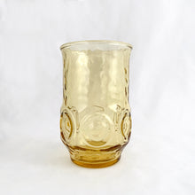 Load image into Gallery viewer, Vintage retro "Heritage Hill" honey gold 6 oz flat juice glass. Crafted by Anchor Hocking, USA, circa 1976. These glasses feature a textured finish with 6 embossed circles around the body, a flared top and tapered base. Perfect for the bevvy of your choice...cheers! In excellent condition, free from chips, minimal wear. Measures 2 1/4 x 3 3/4 inches Capacity 6 ounces