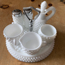 Load image into Gallery viewer, This rare vintage "Hobnail" milk glass condiment set features a round tray with silver-toned handle, salt and pepper shakers, cruet with stopper, creamer, open sugar and jam pot. A classic piece of American glass history to add to your collection! In overall excellent condition for a set of this age. Absent from this set are the lid and spoon for the jam pot. The lid on one of the shakers has damage in one spot where the chrome finish has come away (see photos).