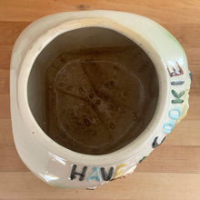Load image into Gallery viewer, This rare vintage ceramic corner cookie jar features brunette and blonde cheerleaders in old-fashioned outfits, cheering underneath the words Have A Cookie in between is a megaphone on the grass that reads cookie time all glazed in shades of green, blue, yellow brown and black on a cream ground, topped with a rust-brown megaphone on the lid. The piece-de-resistance are the cheerleaders holographic facial expressions that change from eyes open with a wide smile to eyes shut with closed smiles.