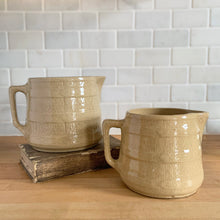 Load image into Gallery viewer, Vintage natural yellow ware strapped barrel milk pitcher featuring navy lily in bas relief with rope style handle, No. 21171. Crafted by Robinson Ransbottom Pottery Co., USA, 1930s. Enhance your home's decor with this beautiful piece of primitive farmhouse tableware. A wonderful addition to any art pottery collection!
Excellent vintage condition, no chips/cracks/repairs, age-related crazing and typical manufacturer's glaze pops. Unmarked
Option 1: 4 x 4 1/8 inches. 32 oz
Option 2: 5 1/4 x 5 1/4. 48 oz