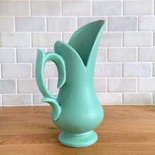 Load image into Gallery viewer, Rare vintage mid-century matte turquoise vase with decorative handle. Crafted by McCoy Pottery, 1950s. This vase is must for any art pottery collector! Makes a perfect mid-century decor statement or give as a gift.
In good condition, slim chip to the handle, no cracks/repairs. Maker's mark on the bottom.
Measures 6 x 9 inches (incl. handle/spout)
