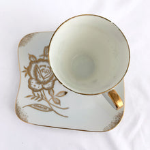 Load image into Gallery viewer, This vintage white porcelain teacup and saucer is absolutely stunning! The unique polygon shaped saucer and teacup are decorated with hand painted gold gilt roses and details. Produced in Japan. In good vintage condition, free from chips, cracks and repairs. Marked "Oakwood Hand Painted Japan". Teacup measures 3 3/14 x 2 3/4 inches | Saucer measures 5 3/4 x 5 x 5 3/4 inches
